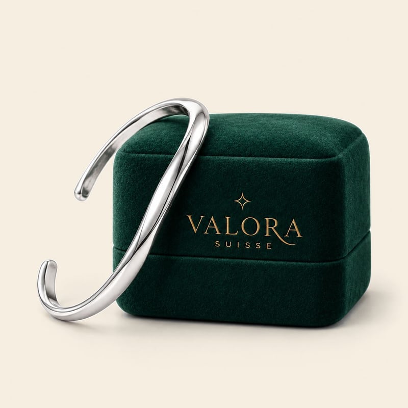 Bracelete aberto de linhas orgânicas e acabamento polido, apoiado em um estojo de veludo verde com o logo Valora Suisse.
